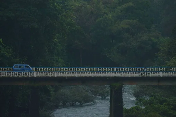 一辆蓝色的复古面包车停在一条被树木环绕的河上的桥上 — 图库照片