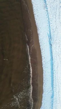 Güneşli bir günde dalgalı karlı bir plajın havadan çekilmiş görüntüsü.