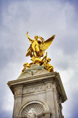 Kraliçe Victoria Memorial 'ın düşük açılı çekimi. Londra, Buckingham Sarayı yakınlarında bulutlu gökyüzünün altında altın kanatlı bir melek heykeli.