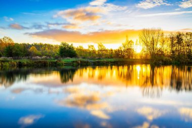 Gölde güzel bir gün doğumu, suda yansıması ve hareket eden bulutlarla.