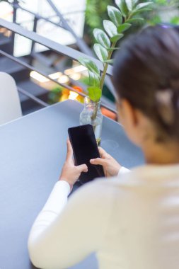 Masanın yanında oturan ve telefonunu kullanan genç bir İspanyol kadın.