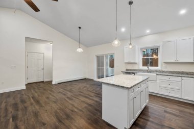 Beyaz duvarları, parke zemini, asılı lambaları ve tezgahı olan bir evin içi.