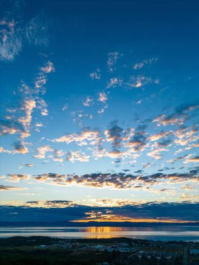 Gün batımında deniz manzarası ve mavi bulutlu gökyüzü ile şehrin dikey görüntüsü.