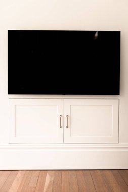 Duvardaki beyaz dolap kapılarının üzerindeki modern bir televizyon ekranının dikey görüntüsü.