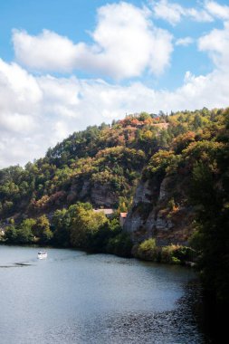 Ormanlarla kaplı, arka planda bulutlu mavi gökyüzü olan bir nehir kenarının dikey görüntüsü.