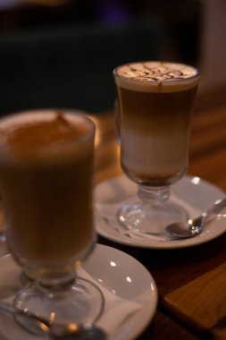 Bir kafedeki ahşap masada iki bardak kapuçino ve güzel bir latte sanatının dikey yakın çekimi..