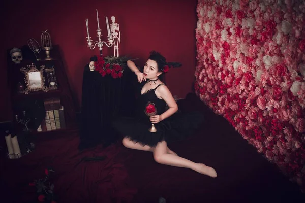 一位美丽的东亚姑娘躺在地上 手里拿着一只玻璃杯里的玫瑰 躺在哥特式的房间里 — 图库照片