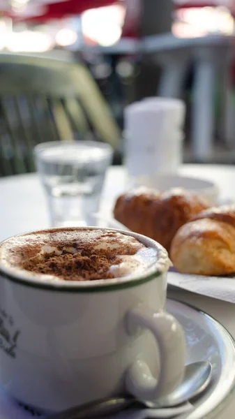カフェの朝食テーブルでカプチーノとクロワッサンのカップの垂直クローズアップショット — ストック写真