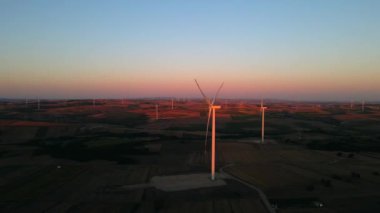 Türkiye 'de gün batımında bir tarlada rüzgar türbinlerinin yavaşça dönüşünü gösteren hava manzarası