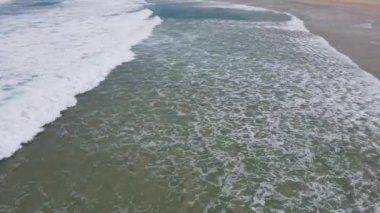 Dalgaların ve kumsalın üzerinden inen bir drone görüntüsü.