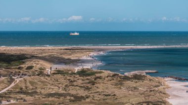 Güneşli bir günde, Skagen kasabasının kumlu sahilinde bir grup insan ve ufukta bir gemi var.