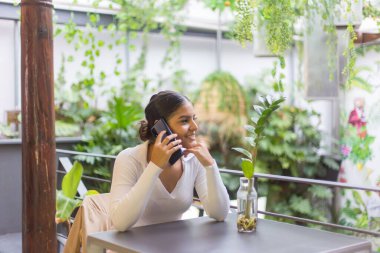 Masanın yanında oturan ve bahçede telefonla konuşan genç bir İspanyol kadın.