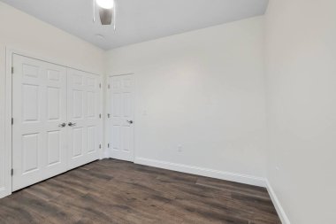 Beyaz duvarları ve üç kapısı olan bir odanın parke zemininin içi.