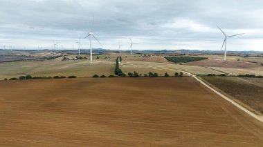 Bulutlu bir günde rüzgâr türbinleri olan bir tarım alanı.