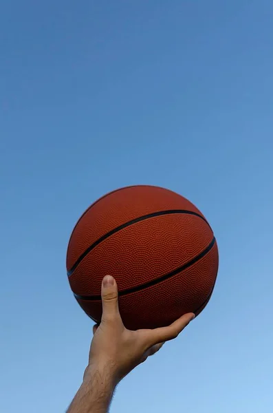 Вертикальний Знімок Червоного Баскетболу Руках Чоловіка Ясним Блакитним Фоном Неба — стокове фото