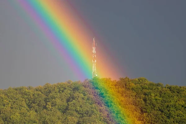 stock image A colorful rainbow on high green mountain under gray sunset sky