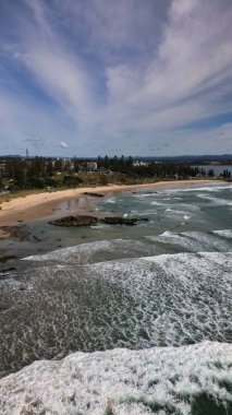 Port Macquarie, NSW 'deki kasaba plajının manzarası, kumlu ve kayalık sahillerde yeşil ağaçlar ve binalar