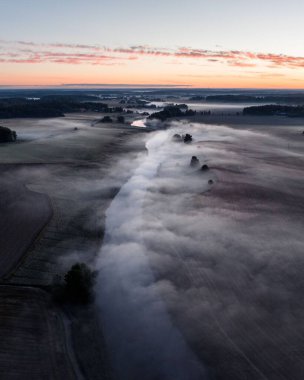 Sisli bir günde uçsuz bucaksız tarım arazisi ve sakin bir nehir manzarası.