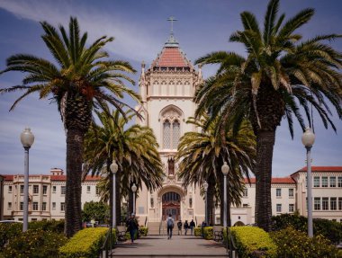 San Francisco Üniversitesi 'nin ön manzarası bulutlu mavi gökyüzünün altında uzun yeşil ağaçlar.