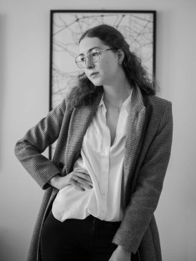 Duvardaki çerçeveli bir sanat eserinin arka planında poz veren bir kadının dikey gri pulu.