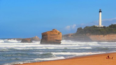 Biarritz, Fransa 'da dalgaların kayalık kıyıya vurduğu nefes kesici bir deniz feneri manzarası