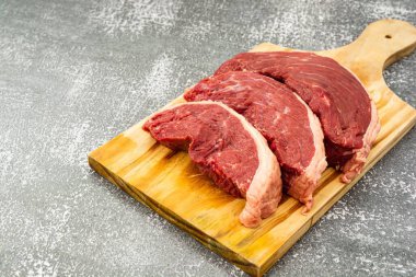 Tahta kesme tahtasında çiğ Picanha bifteği ve gri bir masanın üst görüntüsü.