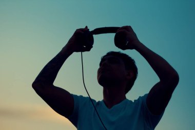 Gün batımında kulaklık takan genç bir adam. Arka planda güzel bir gökyüzü var.