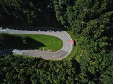 Avusturya 'da ağaçlarla çevrili kırmızı ven ile kaplı kıvırcık bir yolun insansız hava aracından güzel bir üst manzara.
