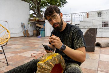 Cadılar Bayramı için balkabağı delen dönen bir aletle tozla kaplı gözlüklü genç bir adam.