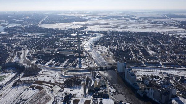 An aerial shot of a city, with a frozen river and snowy fields on a cloudy winter day