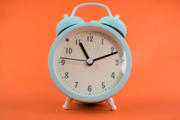 オレンジ色の背景に青い目覚まし時計の孤立したショット — ストック写真