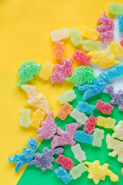 一只呈恐龙状的彩色糖果和一只被酸性粉末覆盖的熊在五彩斑斓的背景上的垂直平面照片 — 图库照片