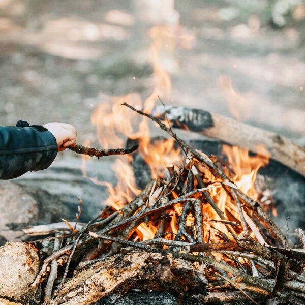 A hand holding a twig and playing with the campfire