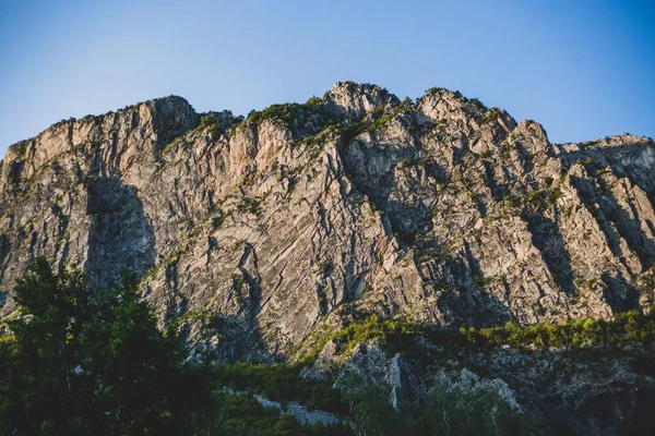 蓝色的天空下 山坡上的树木正对着一个巨大的岩石悬崖 — 图库照片