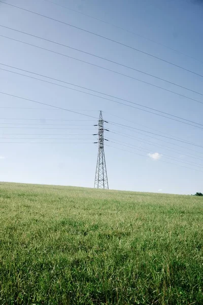 田舎の緑のフィールド上の電気線と高電圧鋼パイロンタワーの垂直ショット — ストック写真