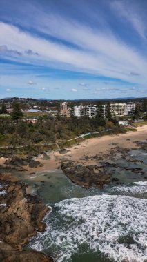 Port Macquarie, NSW 'deki kasaba plajının manzarası, kumlu ve kayalık sahillerde yeşil ağaçlar ve binalar