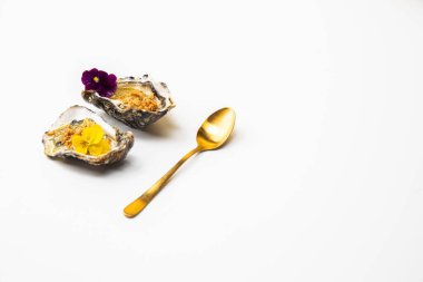 Çiçeklerle süslenmiş istiridyeler beyaz arka planda altın kaşığın yanında duruyor.