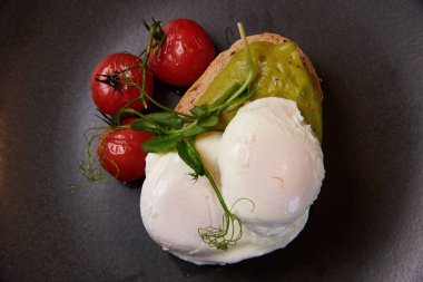 Ekmeğin üzerinde mozzarella peynirinin, siyah tabakta kiraz domateslerinin yanına yakın bir görüntüsü.
