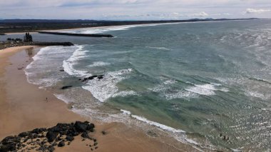 Port Macquarie, NSW 'da kumlu ve kayalık sahillerde yeşil ağaçlı şehir plajı manzarası.