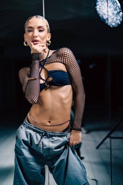Güzel bir kadın dansçının dikey çekimi. Örgü şeklinde poz veren siyah ve bol pantolonlu bir bluz.