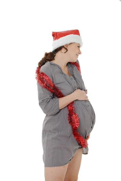 白い背景にサンタの帽子とティンセルをかぶって腹に触れる若い妊婦 — ストック写真