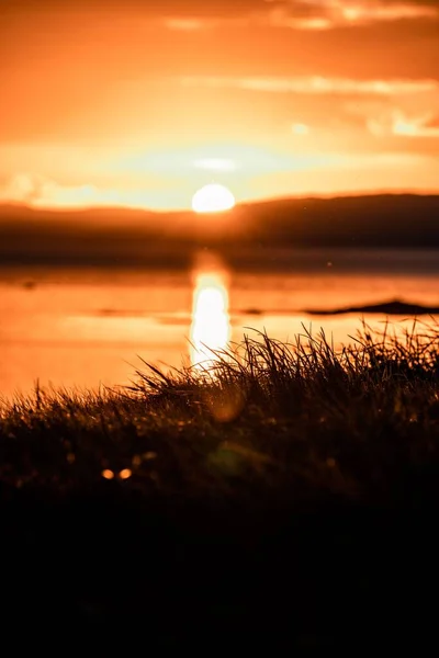 Eine Vertikale Aufnahme Eines Leuchtend Orangefarbenen Sonnenuntergangs Über Dem Wasser — Stockfoto