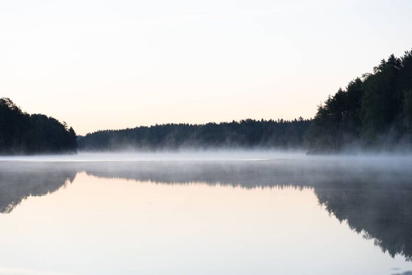 A scenic view of a calm lake and forest during a foggy day