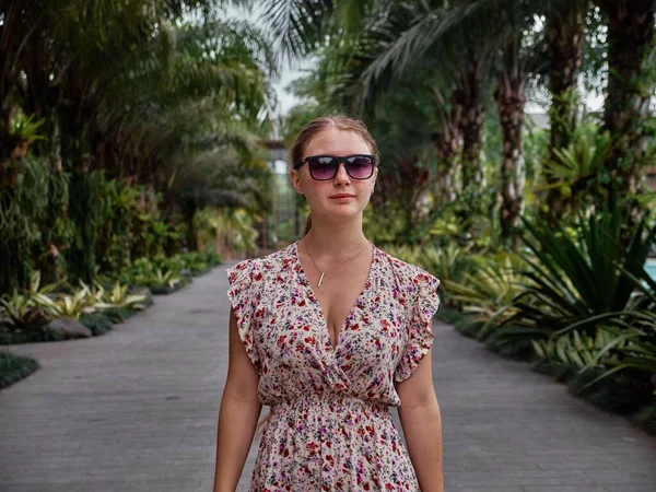 一个高加索女人 身穿花衣 背靠人行道和棕榈树摆姿势 — 图库照片