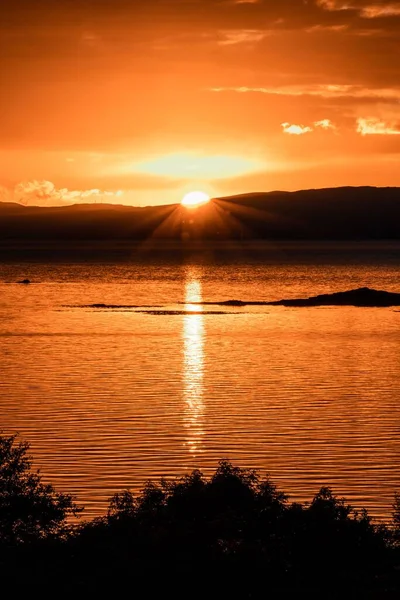 Eine Vertikale Aufnahme Eines Leuchtend Orangefarbenen Sonnenuntergangs Über Dem Wasser — Stockfoto