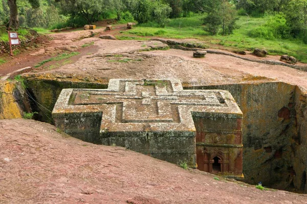 The cross-shaped Rock-hewn Church of Saint George surrounded by green grass and trees in Lalibela, Ethiopia