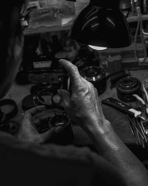 テーブルランプライトの下のカメラ部品を修復する人間の手の垂直グレースケール — ストック写真