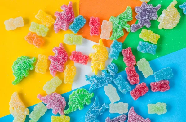 A flat lay of colorful gummy candies in the shape of a dinosaur and a bear covered in sour powder on colorful background