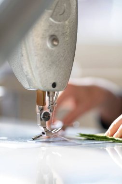 Kesilmiş kadın elleri atölyede iğne ve iplikle makinelere bez dikiyor.