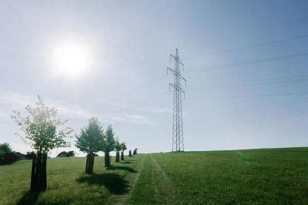 風景の中に送電塔 澄んだ青空の下の緑のフィールドにケーブルラインを持つ高電圧の電柱 — ストック写真